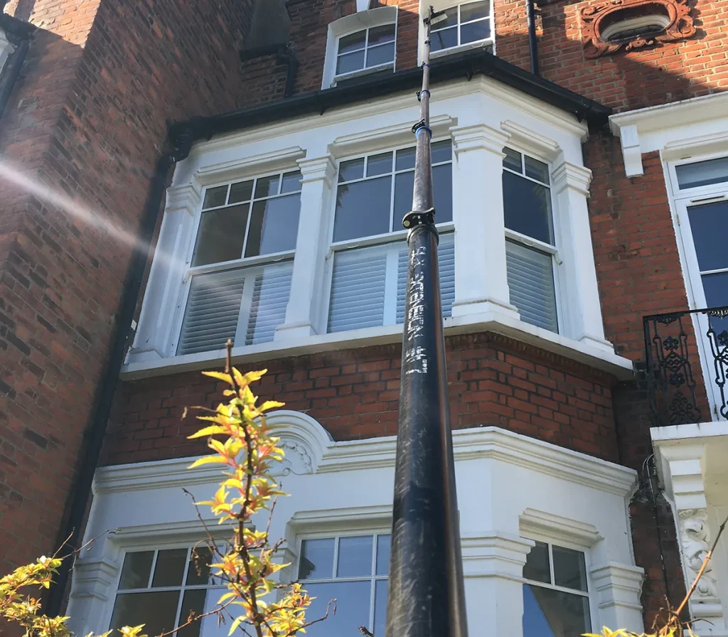 Bay windows on a Victorian house being cleaned with a water-fed pole