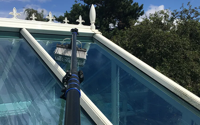 Conservatory roof being cleaned with a pole-fed brush