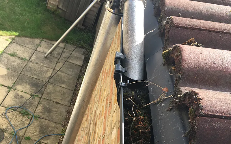 Close-up of a gutter being cleared of moss and leaves